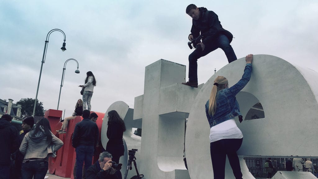 videographer on a video production in Amsterdam shooting downward toward woman climbing the signfrom the top of a sign