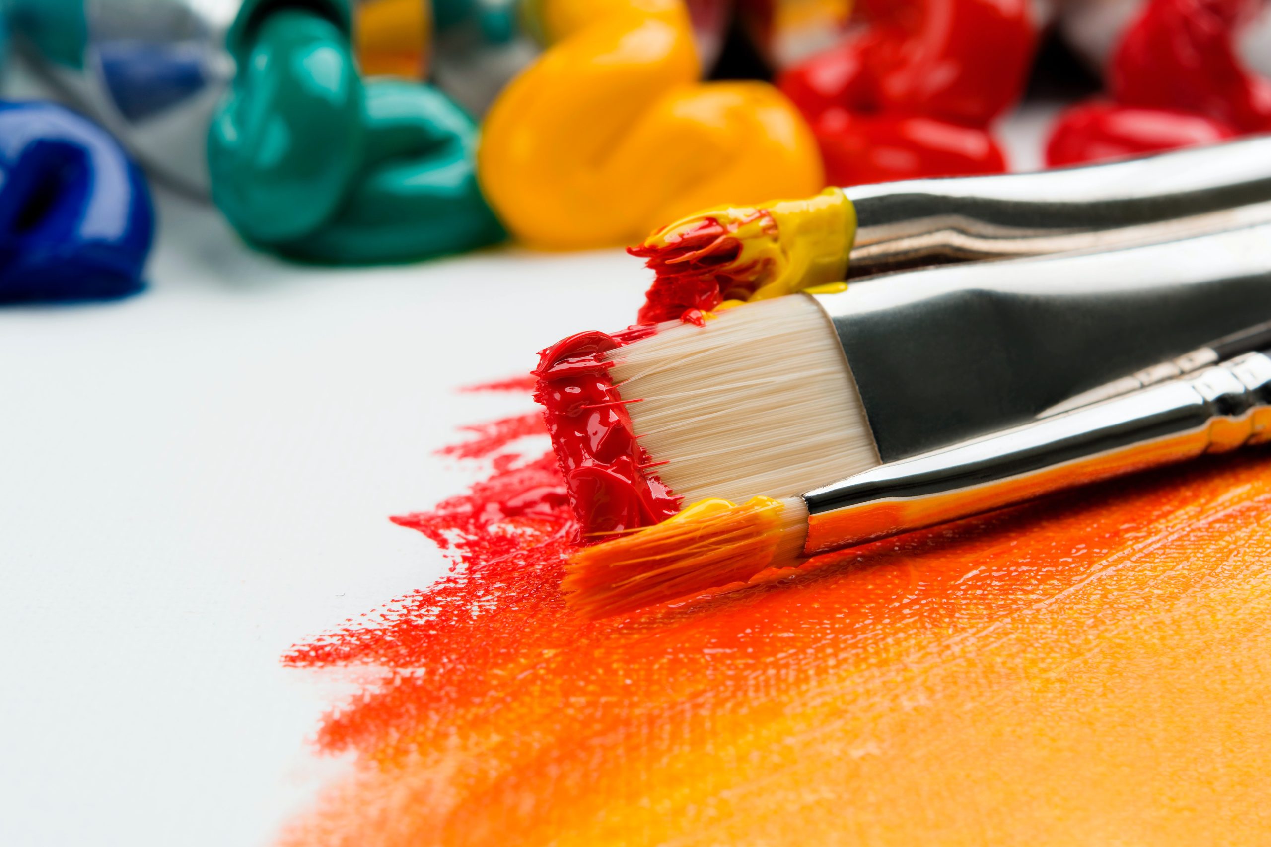 paintbrushes with red and orange paint lying on canvas partially painted