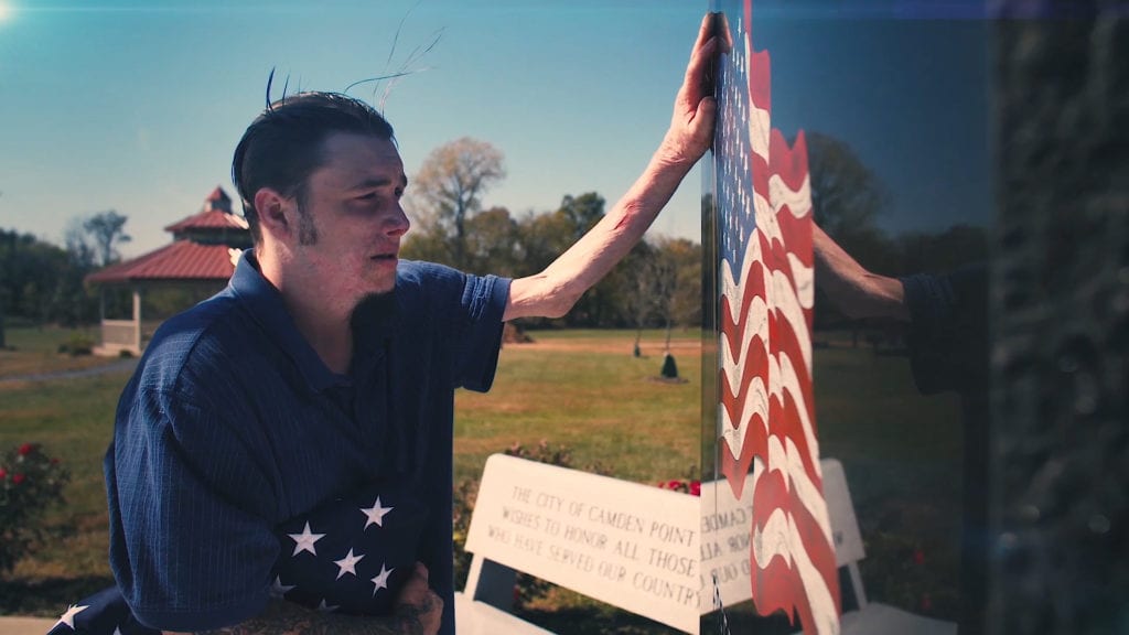 VFW, Veterans, war memorial with man standing in front placing hand on memorial's stone. 