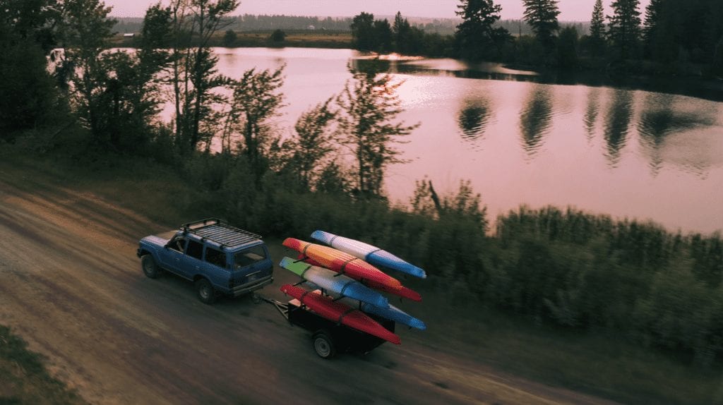 Aerial shot of a blue jeep towing kayaks next to a lake showing scenic road productions going to a shoot