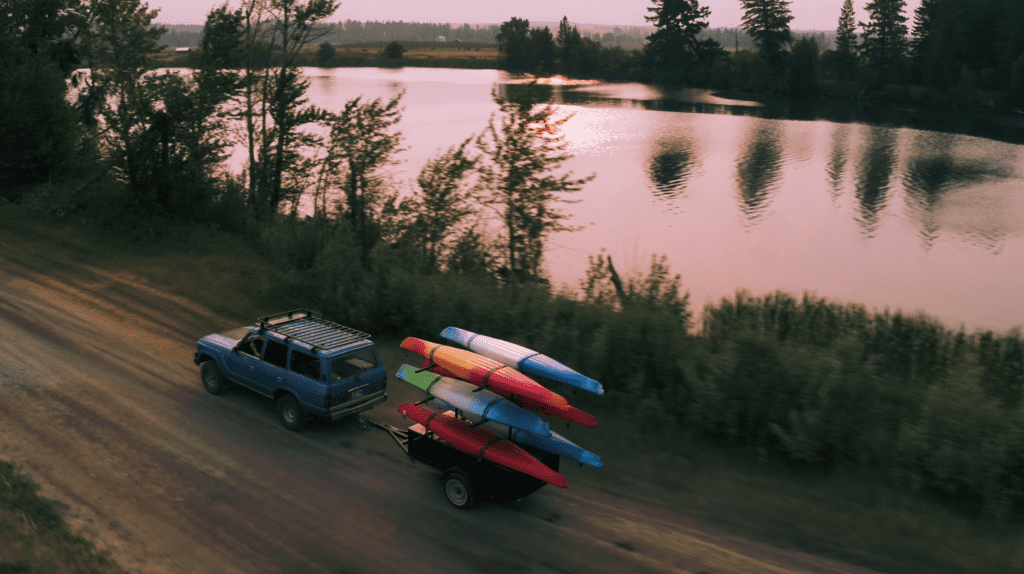 Aerial shot of a blue jeep towing kayaks next to a lake