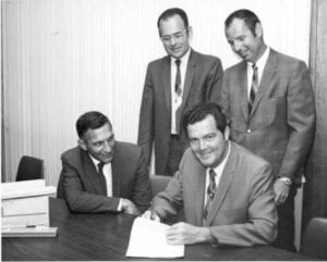 4 white men in suits, corporation founders, looking at a document