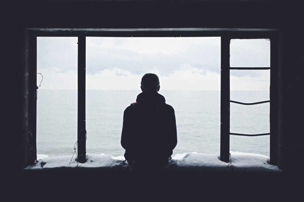 man framed from the back looking out an open window into grey beyond