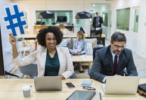 woman holding the pound symbol above her head in an office with coworkers