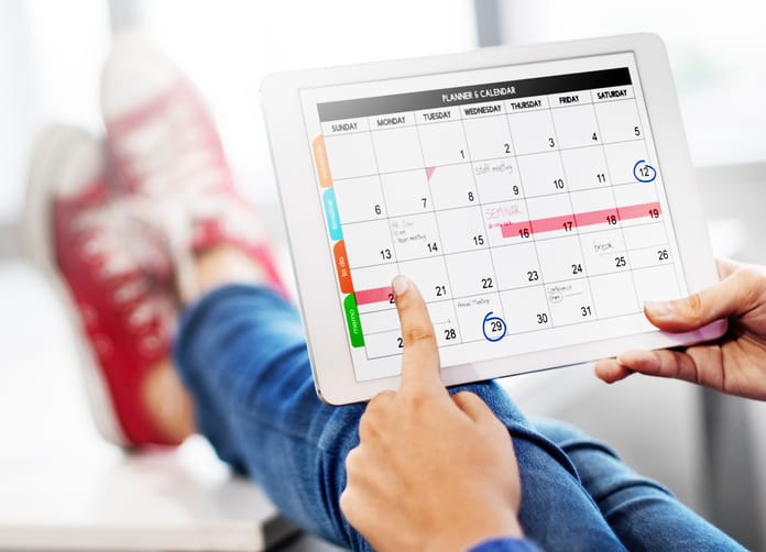 person-with-feet-on-footrest-holding-tablet-displaying-monthly-calendar