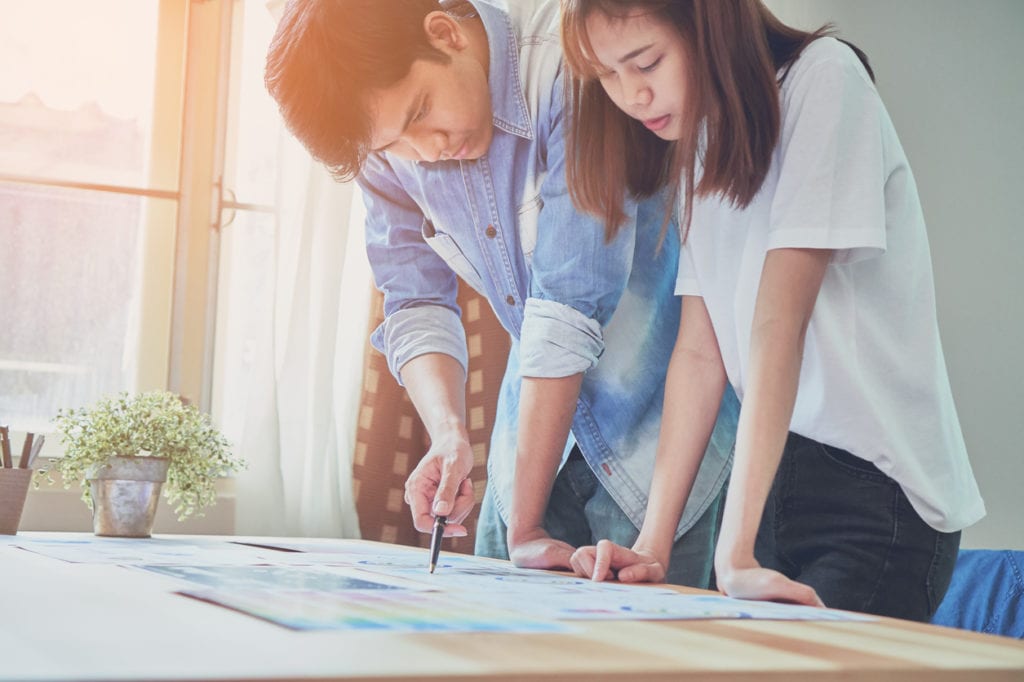 man-and-woman-leaning-over-table-with-papers-while-working-on-project