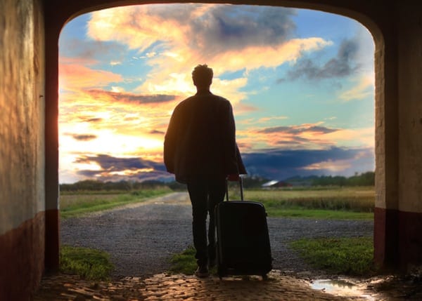 silhouette-of-man-with-suitcase-walking-down-path-towards-sunset