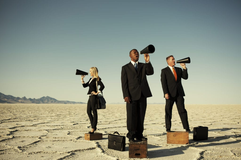 three people in business attire standing in circle with black megaphones in desert