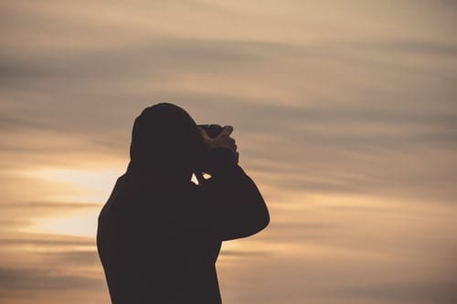 photographer looking through viewfinder of camera at sunset