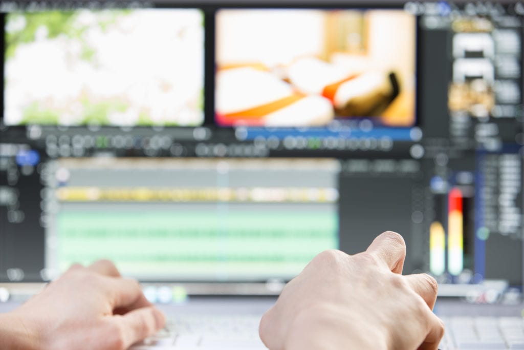 man's hands using keyboard and mouse to edit video on computer monitor