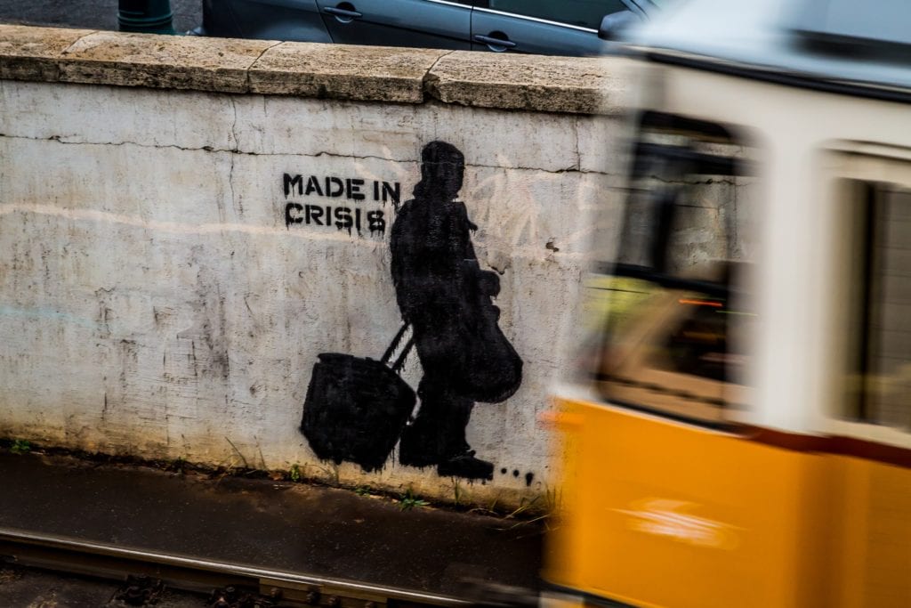graffiti on wall of silhouette of man with suitcase and "made in crisis" text with train in foreground