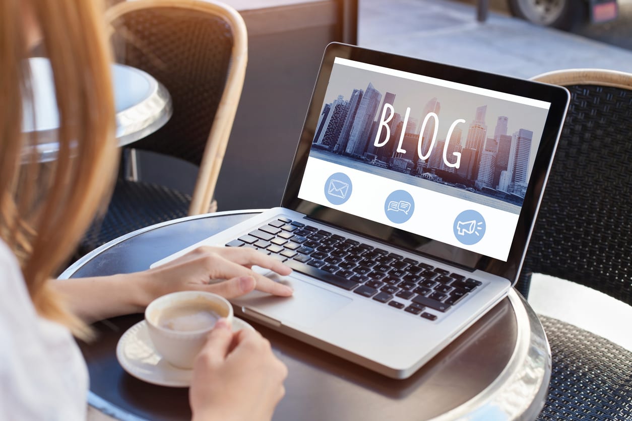 person blogging on computer at cafe table with coffee in hand deciding on her storytelling layouts 