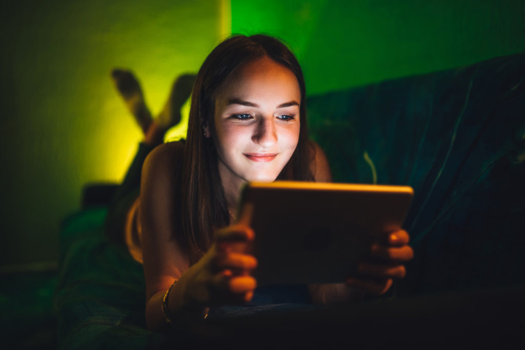 woman lying on sofa in dimly lit room holding tablet with glow from screen illuminating her face