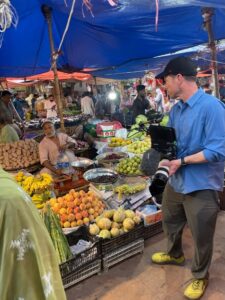 cinematographer stands with video camera in a fruit stand in Pakistan